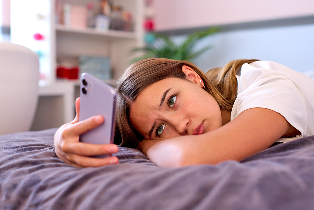 adolescent girl lays on her bed and scrolls through social media